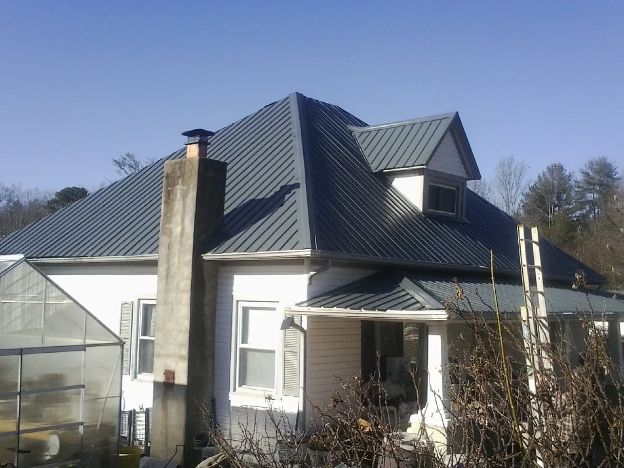 Dark blue standing seam metal roof on a white farmhouse with dormer — Slate & Tile Roof Repair by Roofing Brothers in Hartwell