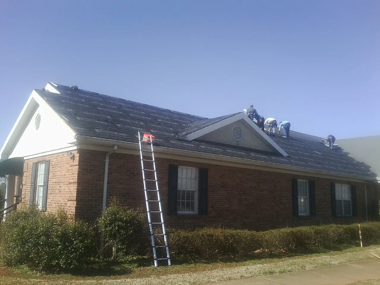Crew tearing shingles off a brick ranch roof with a ladder set — Emergency Roof Repair work by our crew in Hartwell