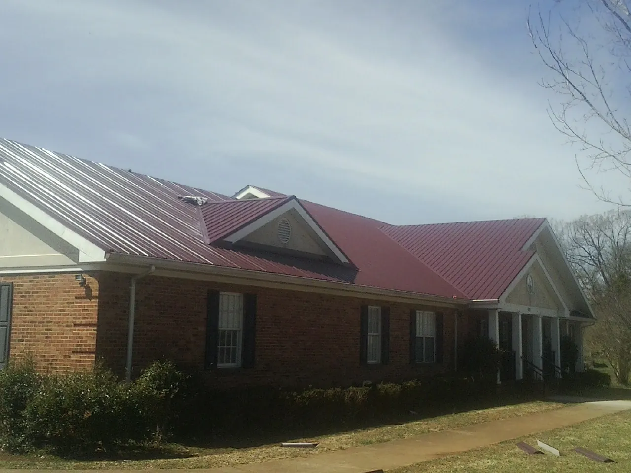 Red metal roof with gabled entries on a long brick building, from a Hail Damage Roof Repair job in Hartwell