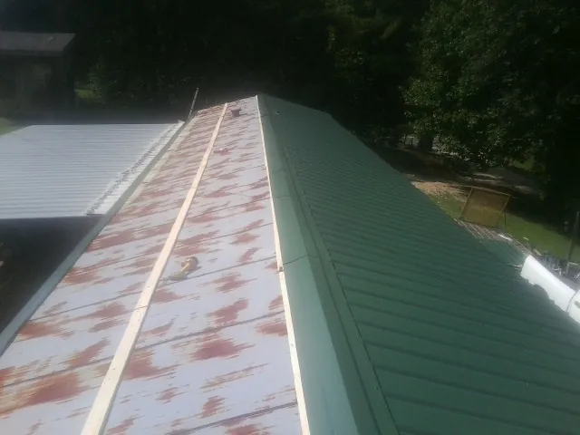 Old rusted panels beside newly installed green metal roofing — Wind Damage Roof Repair by Roofing Brothers in Hartwell