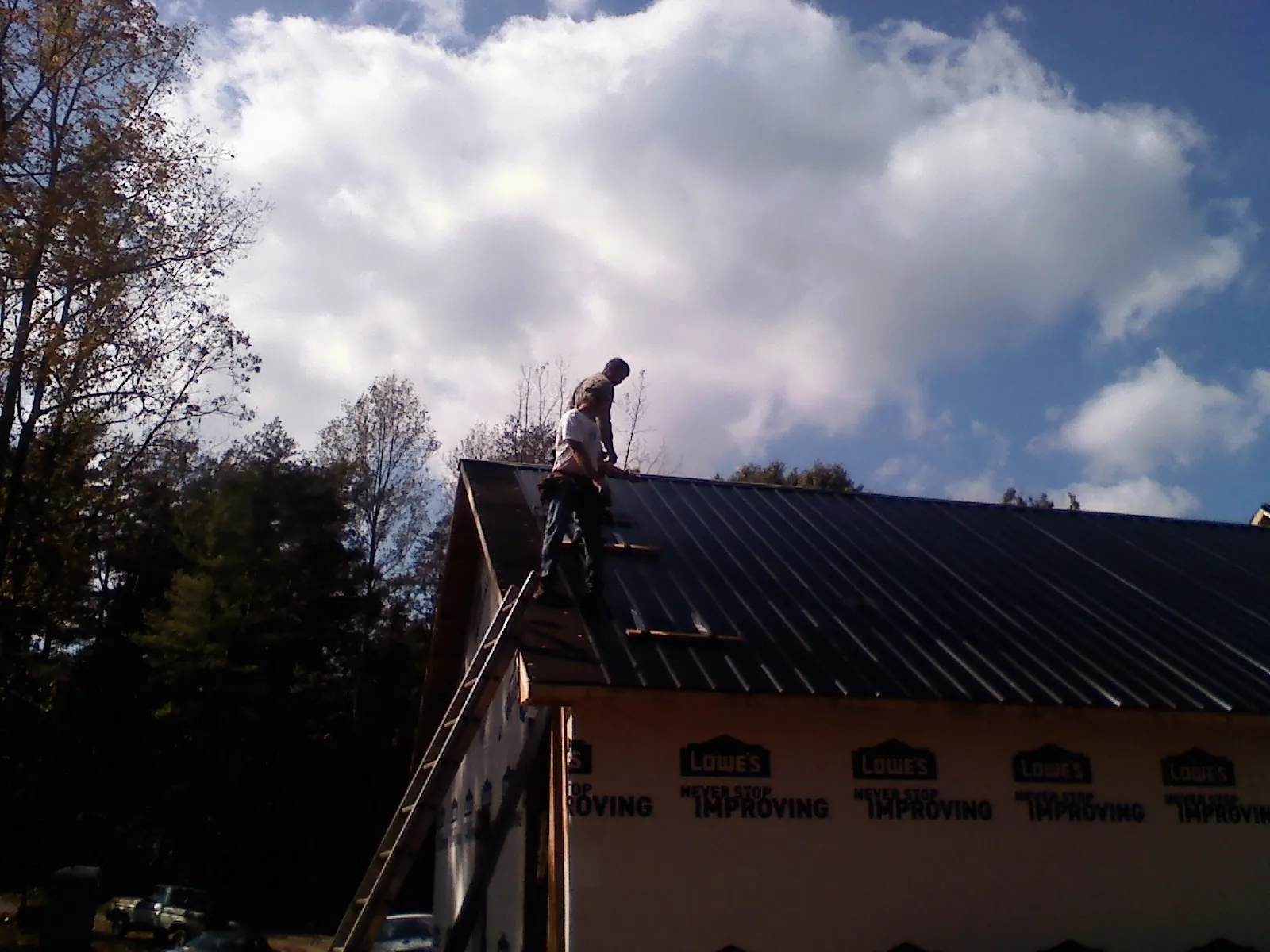 Roofer fastening dark metal panels high against a cloudy sky, from a Roof Inspection job in Hartwell