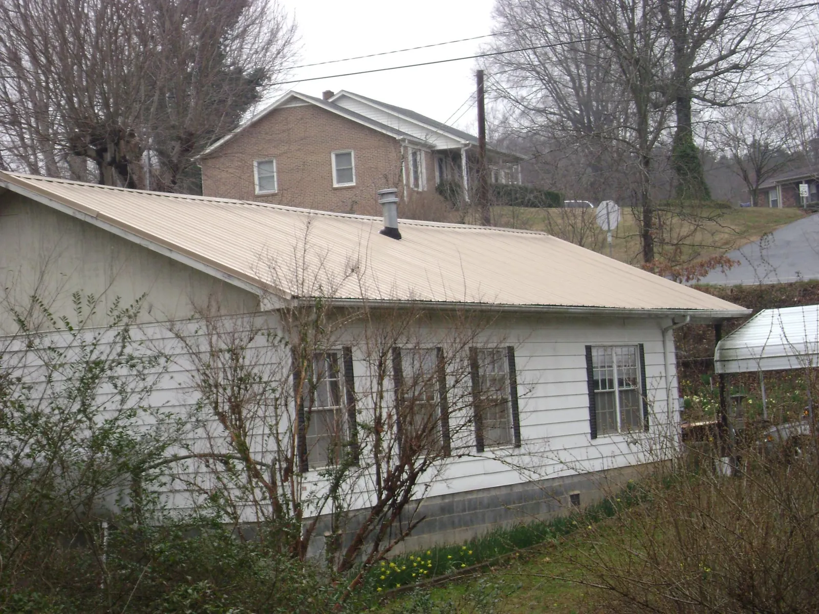 Tan metal roof on a white sided house set into a hillside — Commercial Roofing by Roofing Brothers in Hartwell