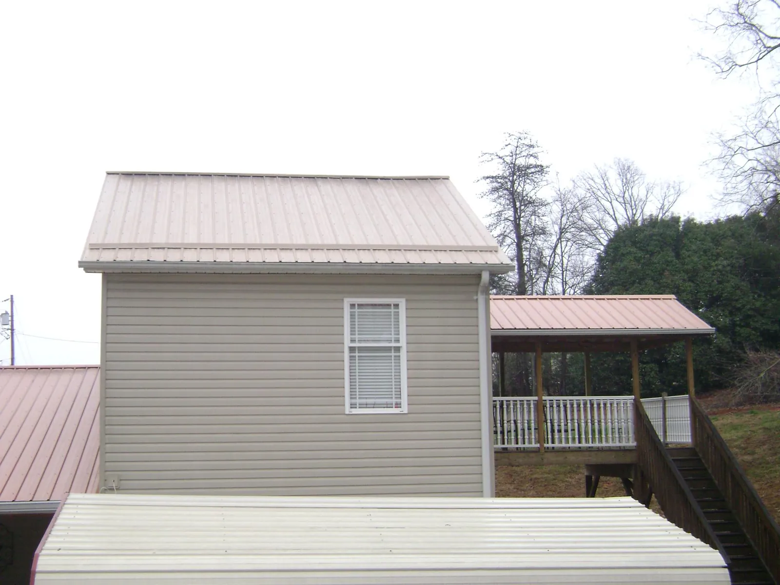 Tan metal roofs on a two story addition and attached porch, from a Roof Replacement job in Hartwell